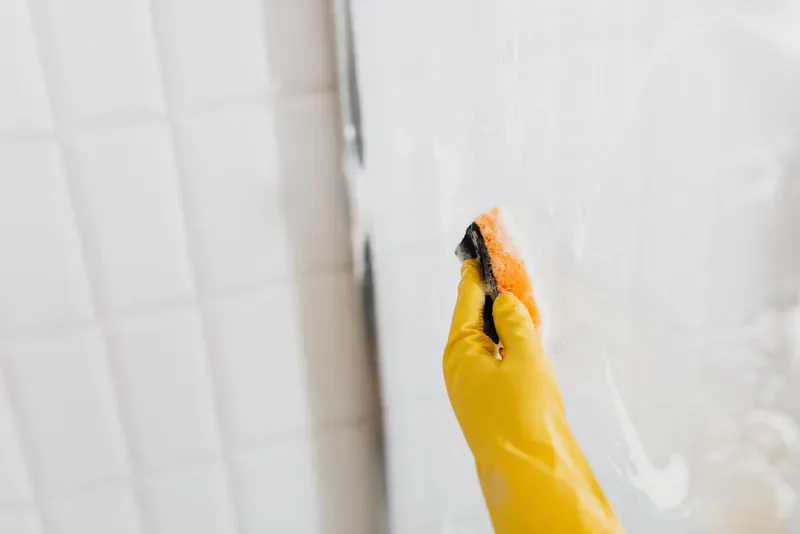 Gloved hand washing hard water film off shower glass during a bathroom cleaning service in Colorado Springs