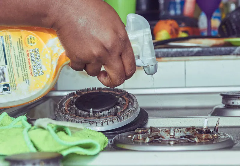 Cleaner degreasing a stovetop with spray and microfiber cloth during a kitchen cleaning service in Colorado Springs